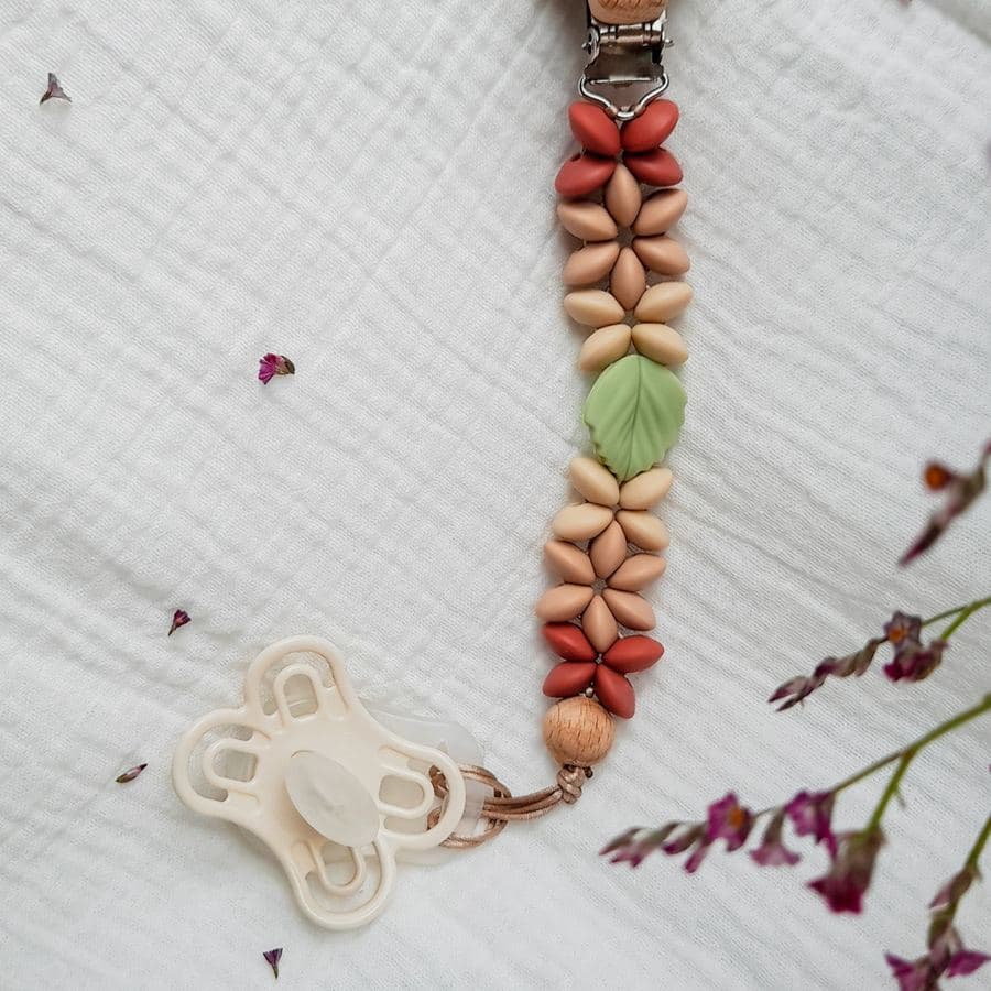 Attache tétine en perles de silicone terracotta, sable et sauge avec une perle feuille, posée sur une mousseline blanche
